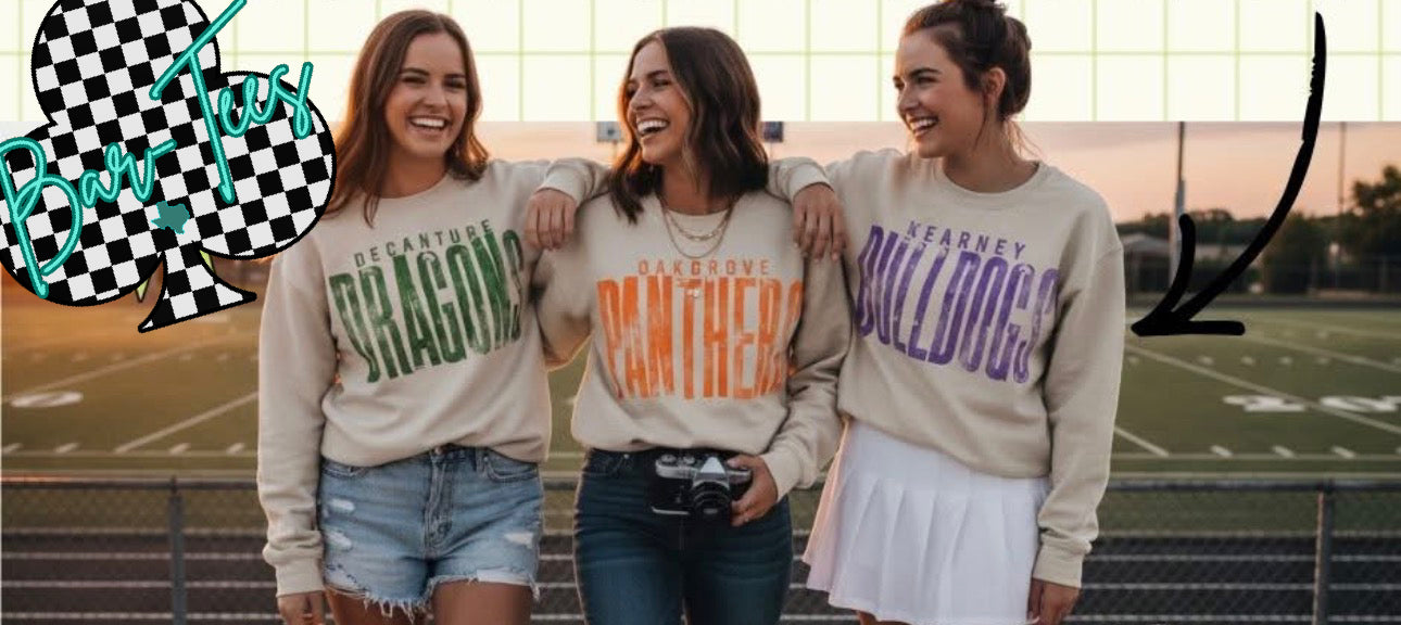 Three women wearing sweatshirts with school names, standing on a sports field.